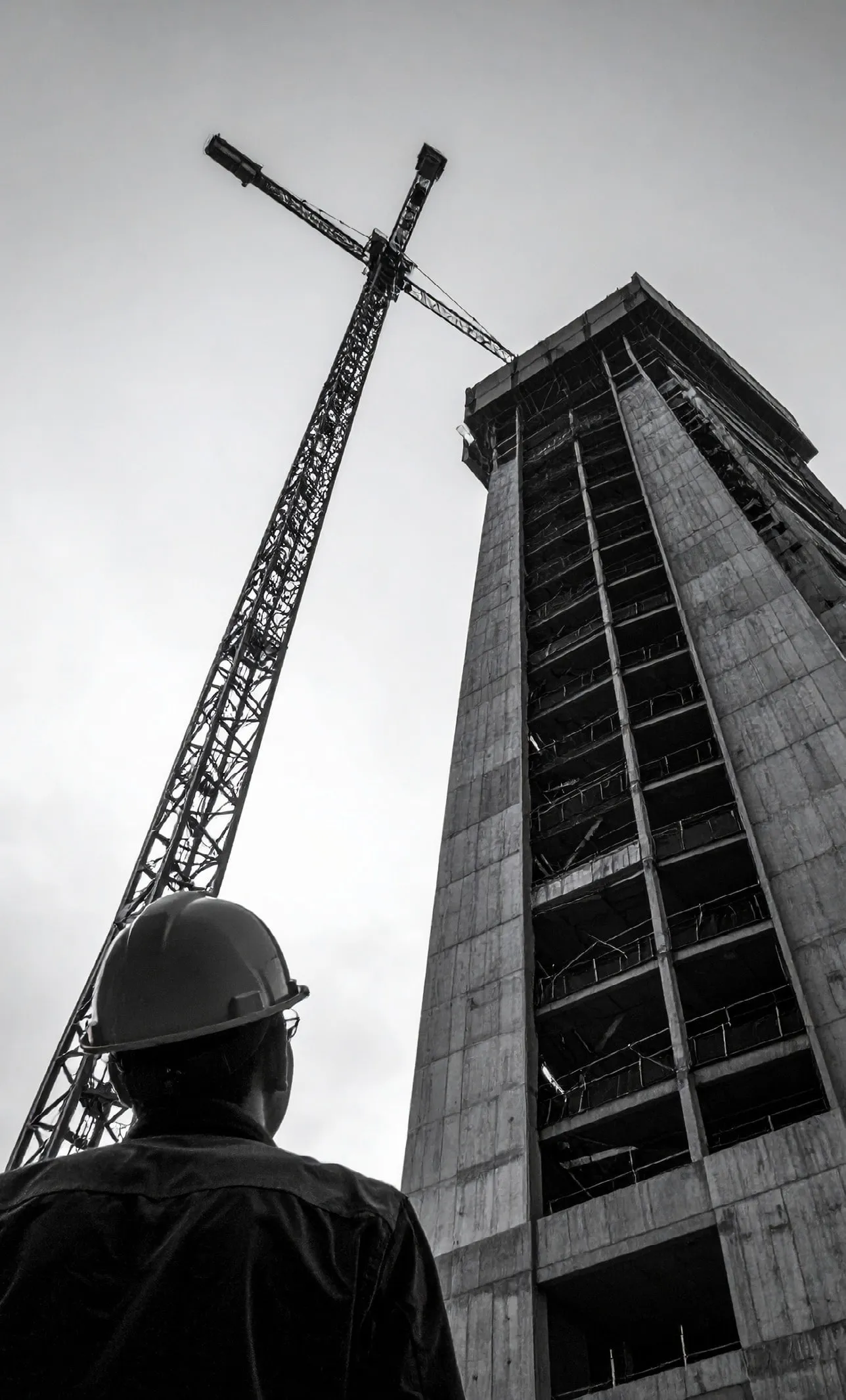 Un chef de chantier casqué observe une tour en construction et sa grue, vue en contre-plongée