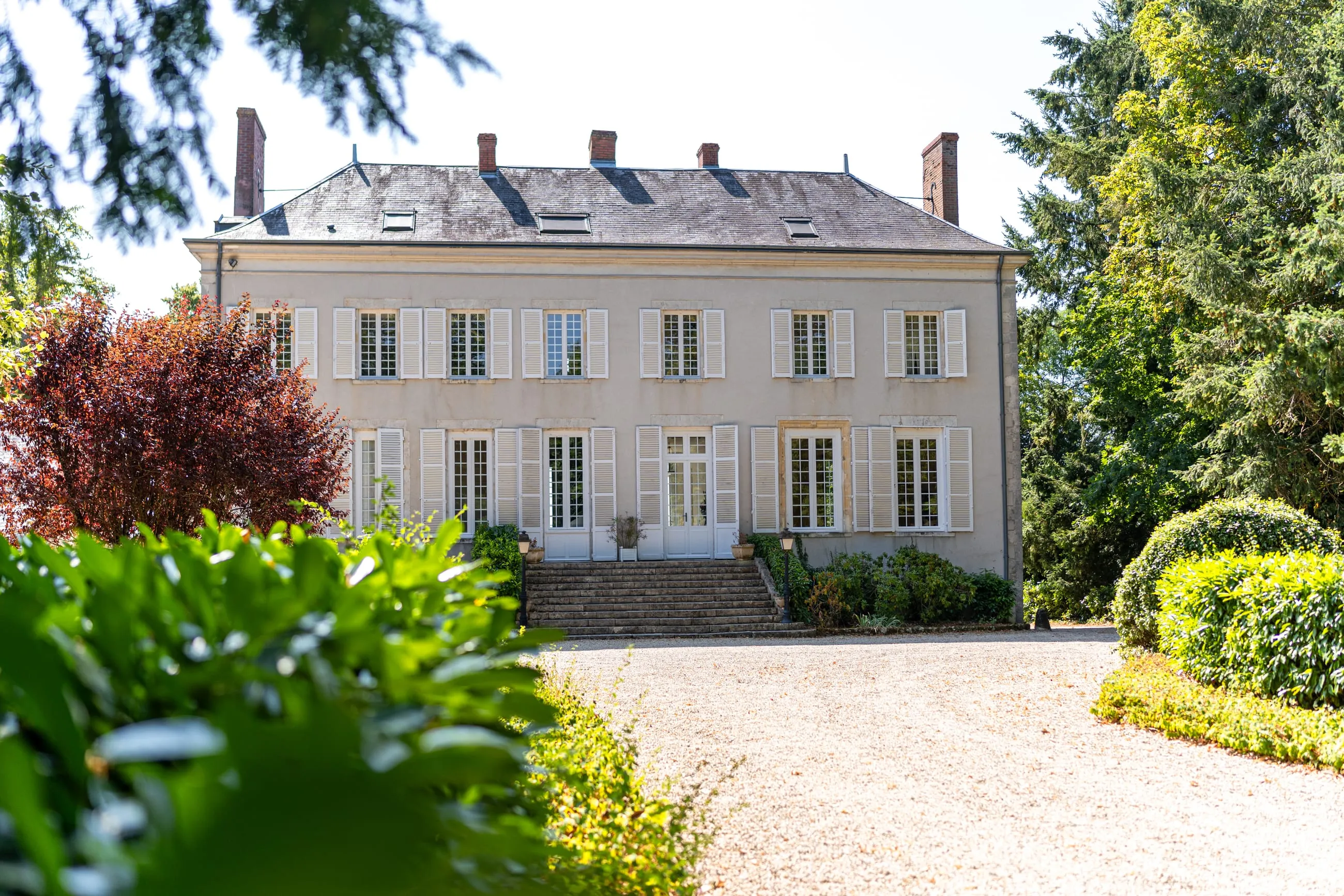 La façade du château, volets clairs et perron de pierre, au bout d'une allée de gravier
