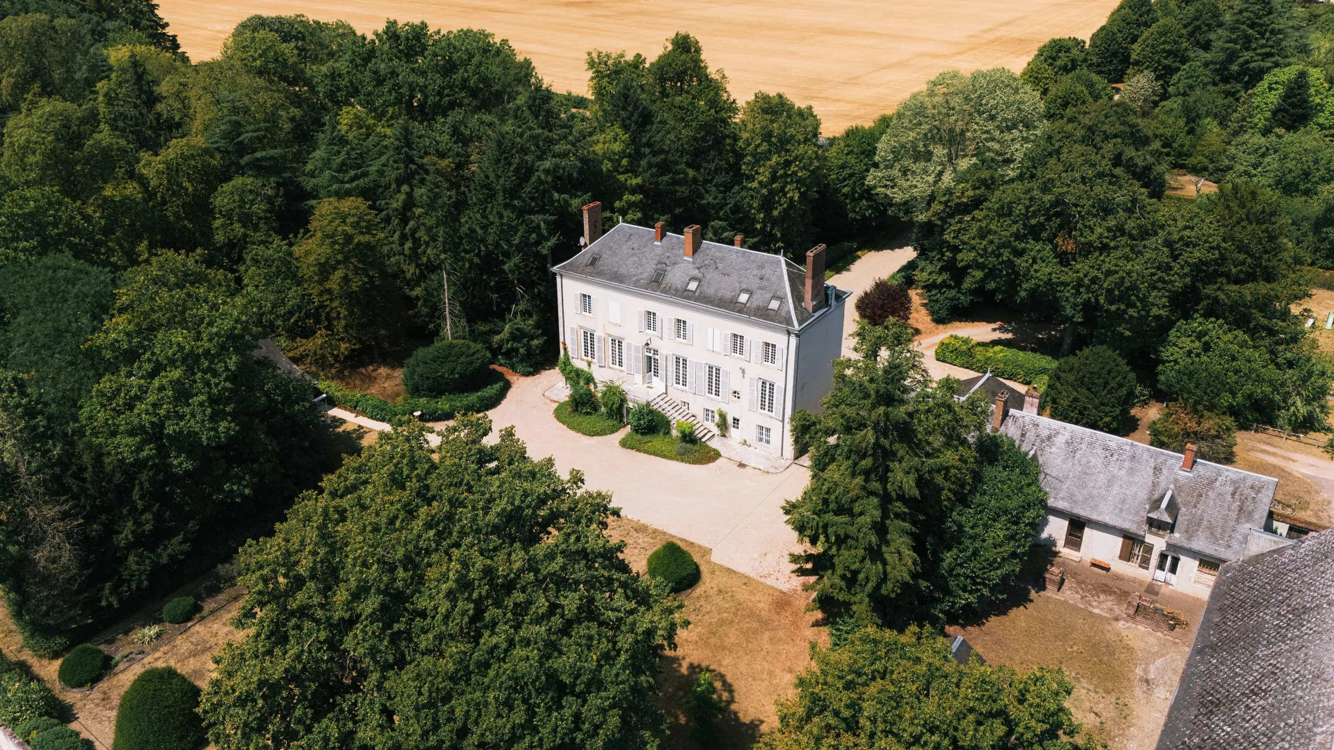 Le château et ses dépendances vus du ciel, au milieu du parc boisé