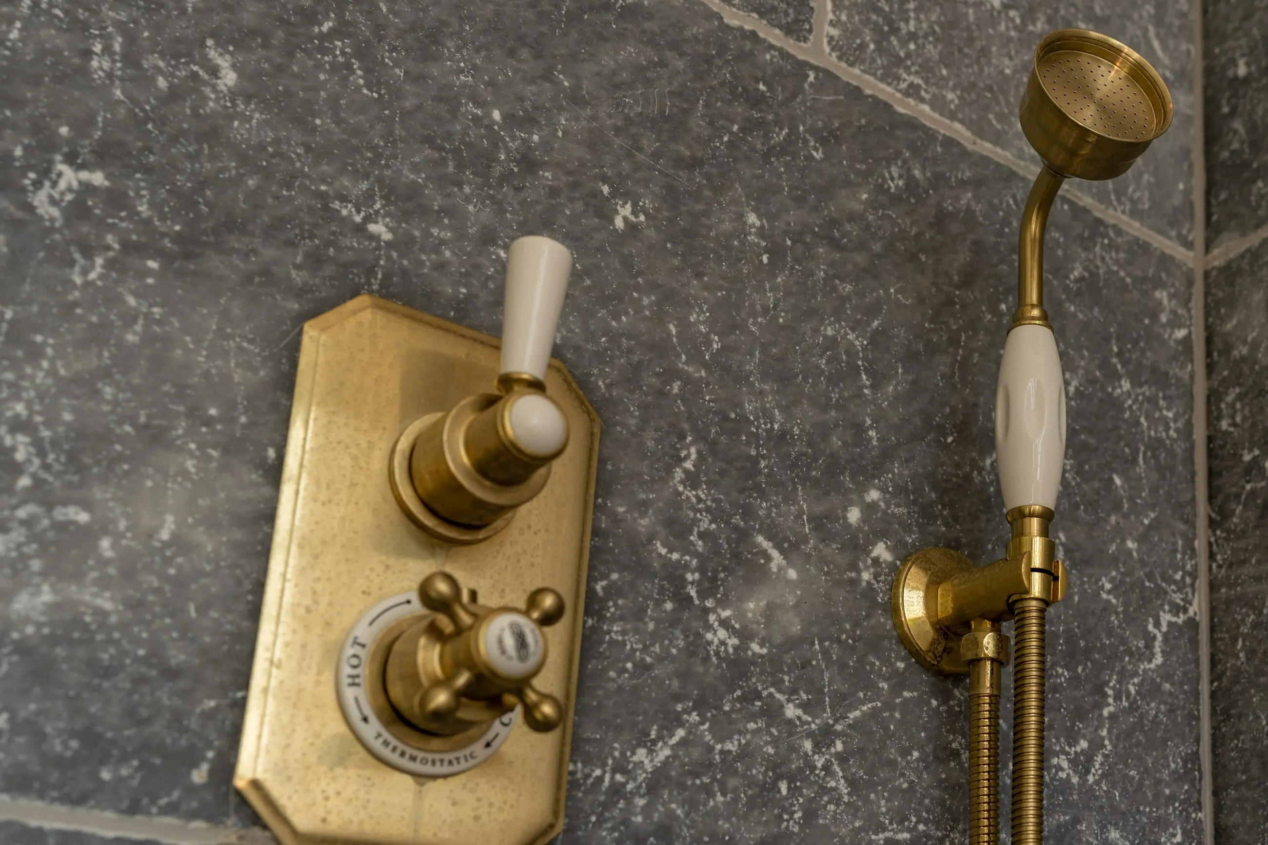 Un mitigeur thermostatique et une douchette en laiton sur un mur de marbre gris
