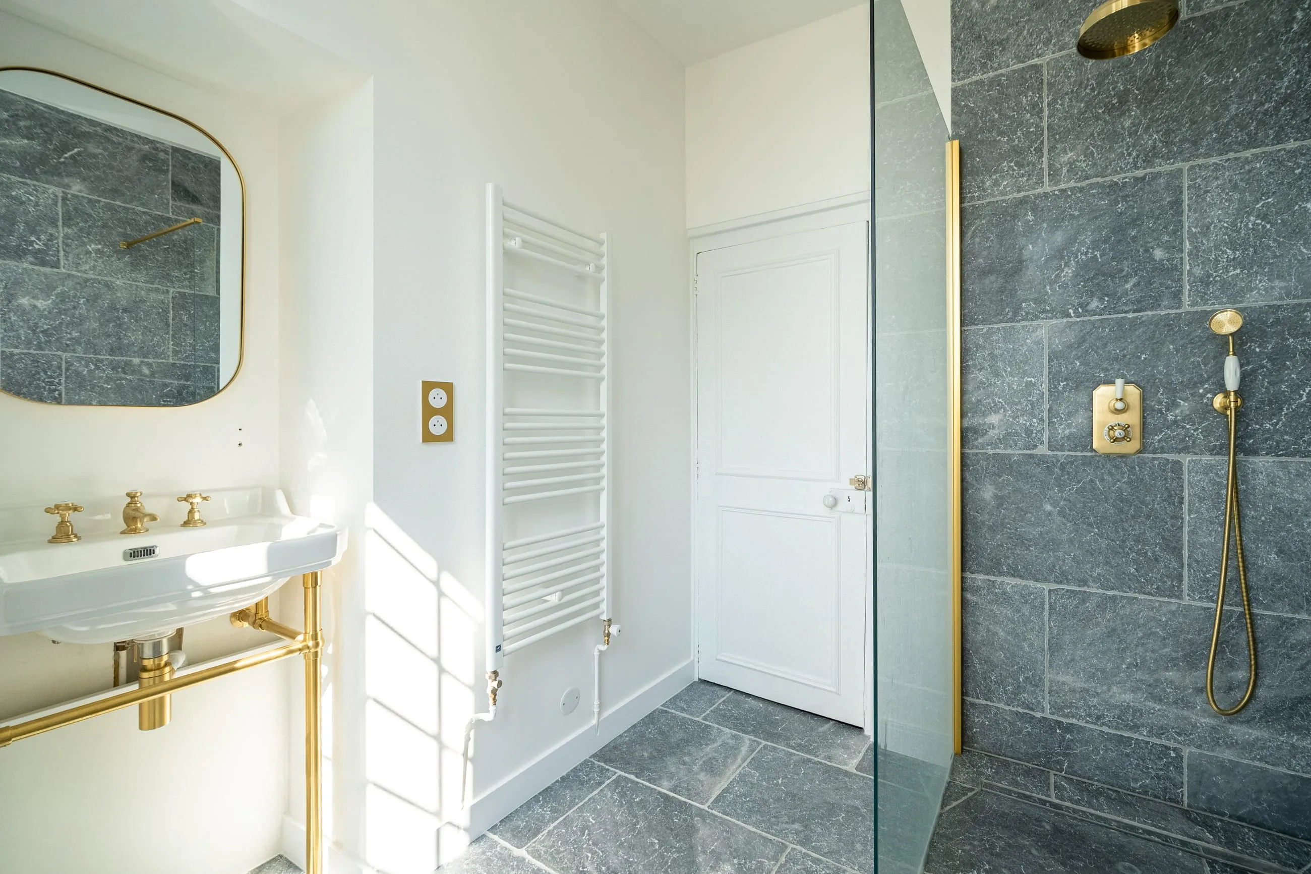 Une salle de bain claire, vasque et robinetterie en laiton, douche à l’italienne en marbre gris